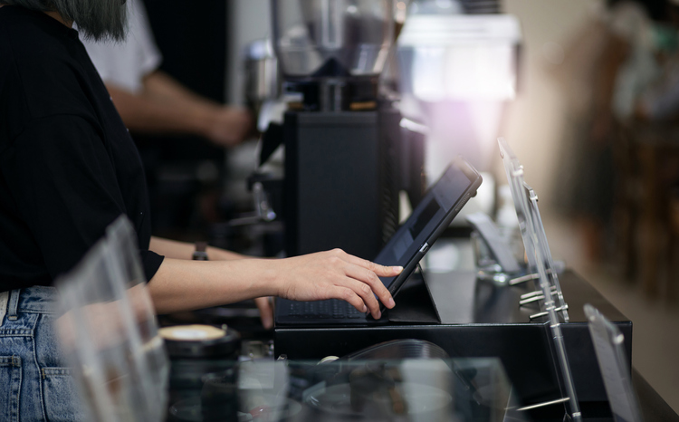 Side view of a young woman touching on the digital tablet to recieve order from customer in coffee shop.