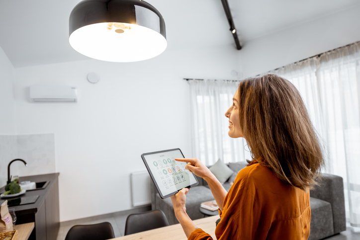 Young woman controlling home light with a digital tablet in the living room. Concept of a smart home and light control with mobile devices.
