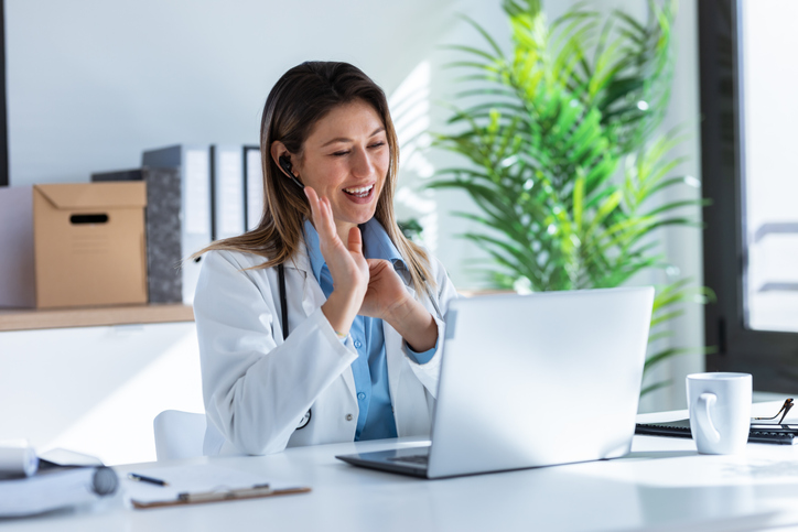  Female doctor talking with colleagues through a video call with a laptop in the consultation.