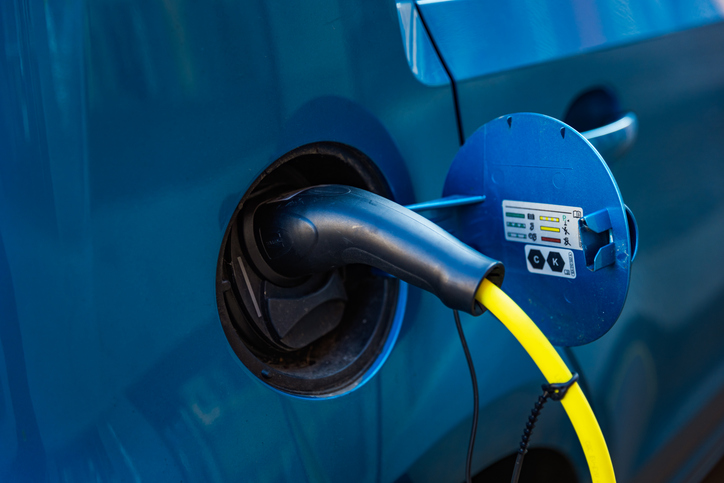 Detail view of a black electric charging cable connected to a blue electric vehicle with a bright yellow cord. The green indicator light is visible, showing that charging is in progress. Perfect concept for clean energy, sustainability, and modern electric transport.