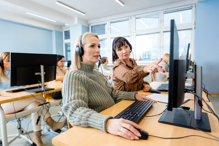 Mature female manager training trainee over computer at office.