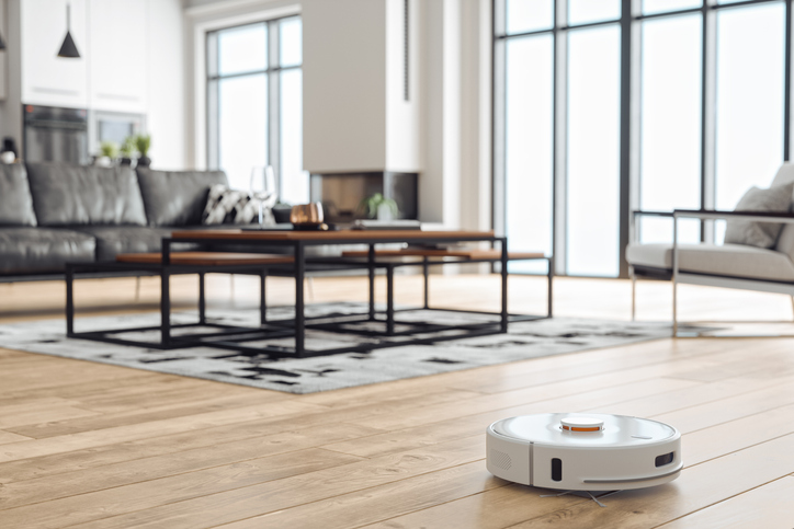 Robotic vacuum cleaner on wood laminate floor in modern home.