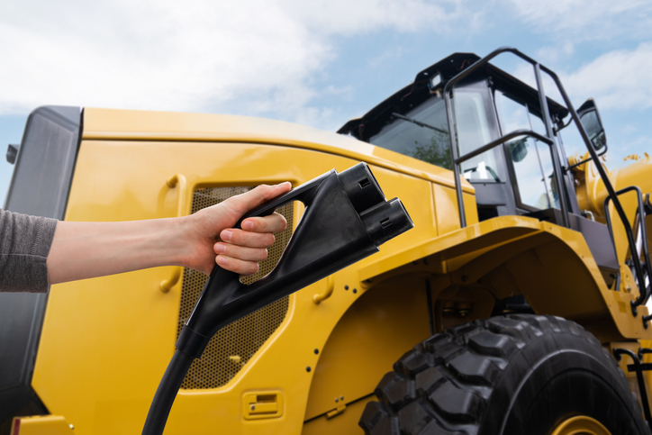Hand with electric vehicles charging plug on a background of electric tractor