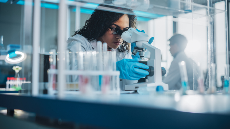 Medical Science Laboratory: Portrait of female scientist looking under microscope to analyze test sample. 