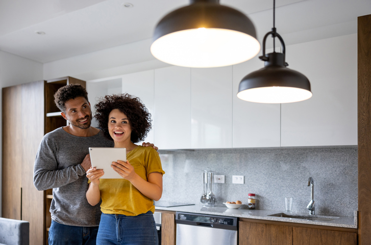 Happy Latin American couple controlling the lights in their house using an automation system on a tablet computer - domestic life concepts.