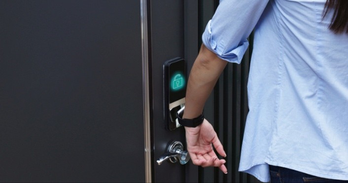 Person holding a smartwatch near an electronic door lock using NFC to unlock it.