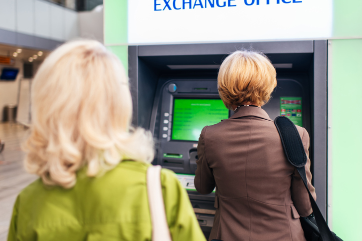 Two senior women using ATM machine at modern bright airport.