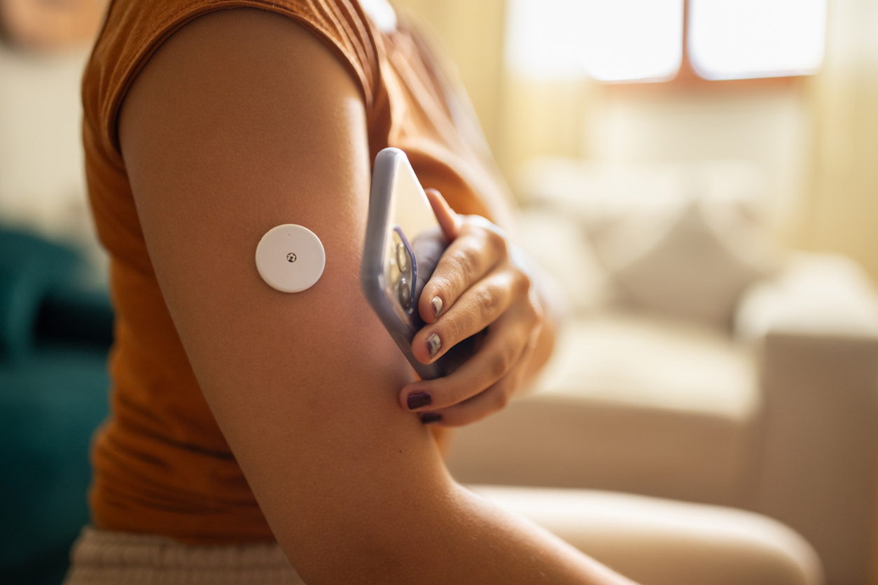 Person at home monitoring glucose with a remote sensor on their arm, scanned by a smartphone.