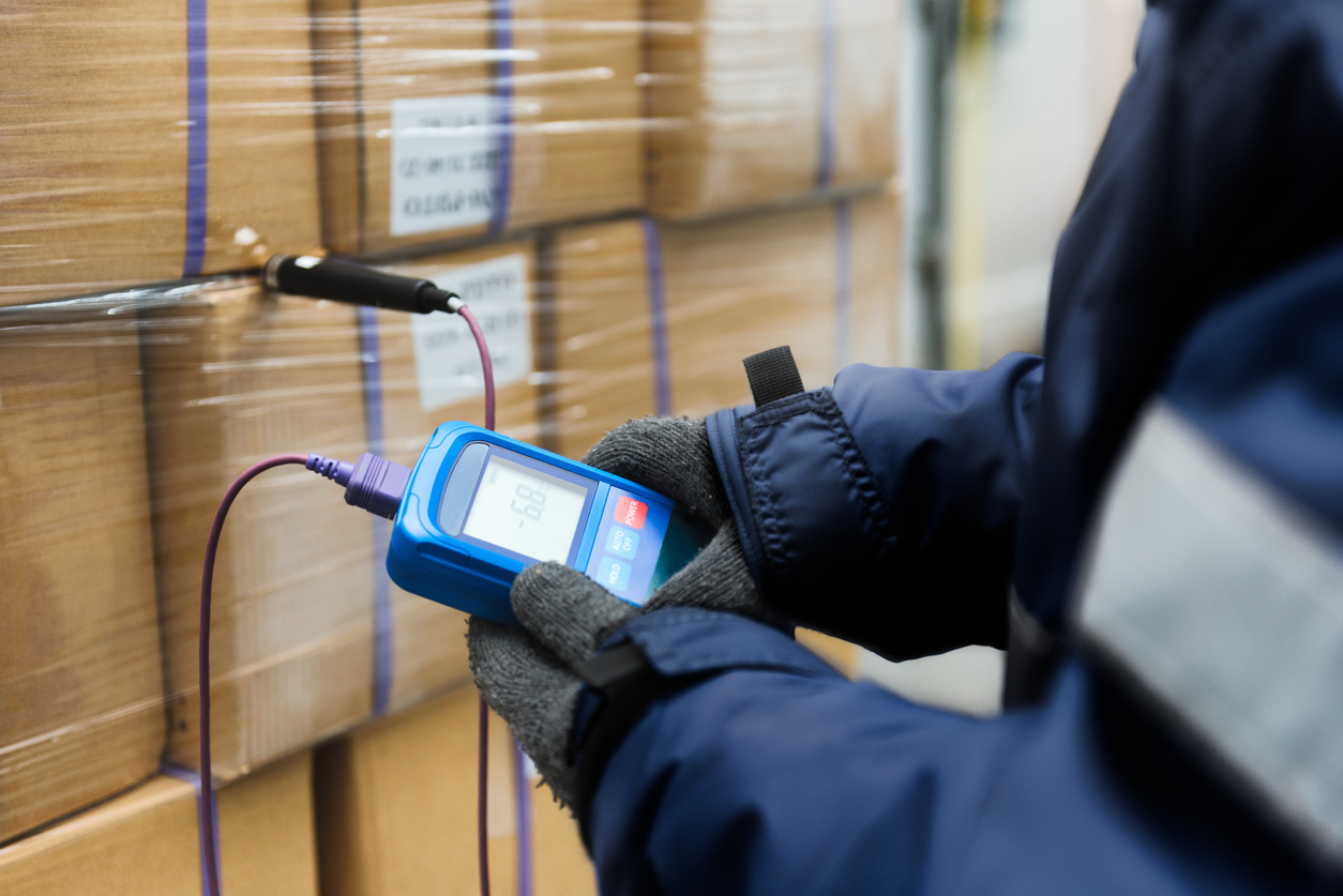 Worker using a thermometer to check the temperature of boxes in a refrigerated warehouse.