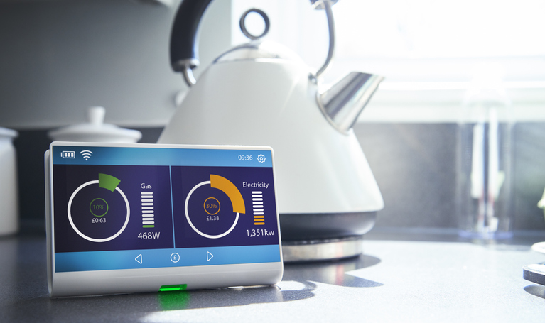 A smart meter on a kitchen work surface showing the households current energy consumption and costs.