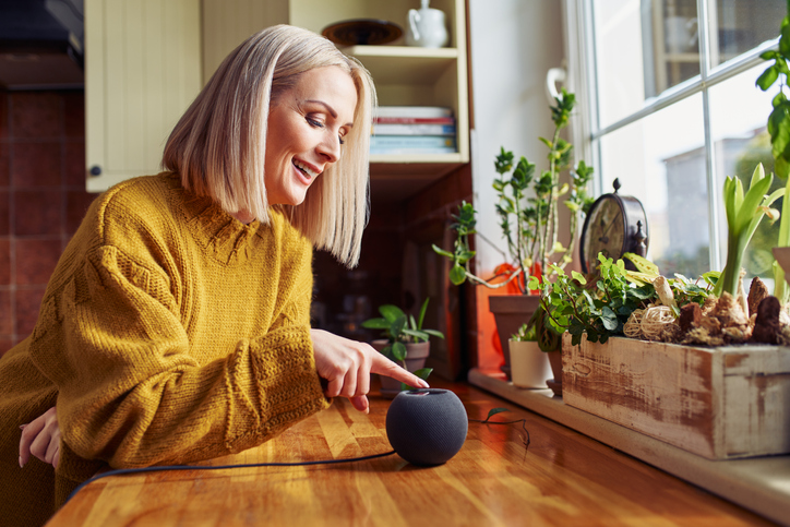 Happy mature woman using smart speaker at home in a kitchen.