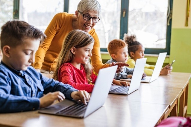 Teacher helping students use computers in an elementary school classroom.
