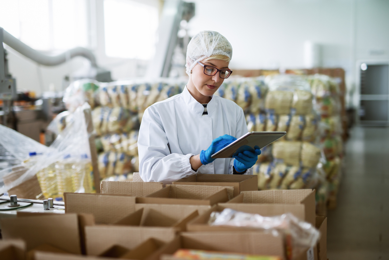  Worker using tablet for checking boxes while standing in food factory.