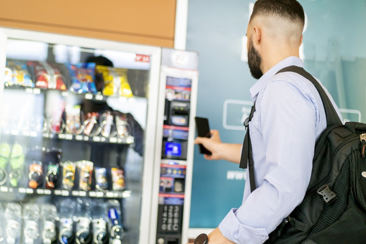 Photo of a businessman in an airport using his phone as payment at a smart vending machine. 